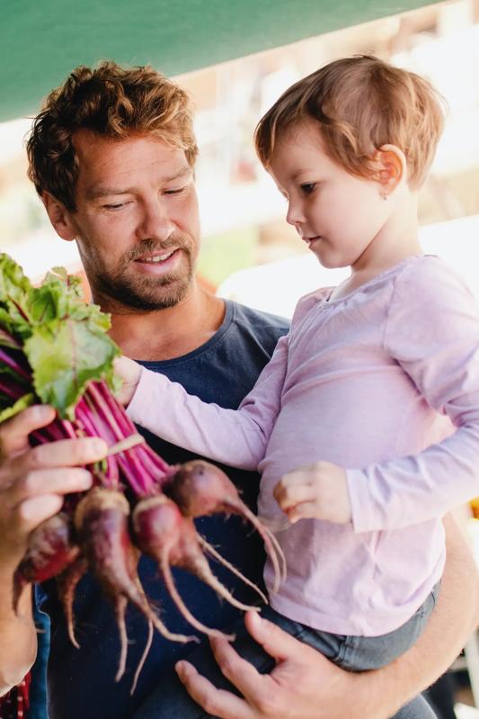 father and young child at a local farmers market holding radishes vespaio apartments