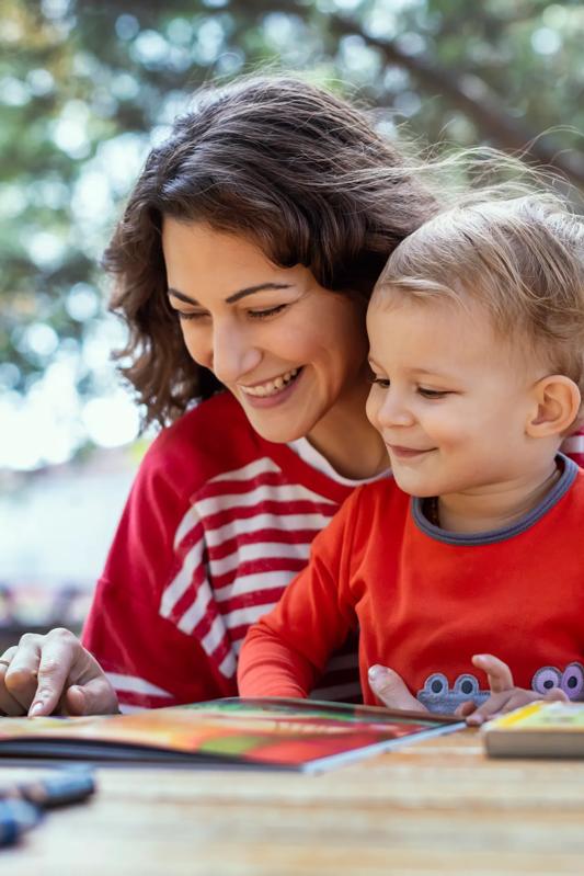 Woman with child outside on table teaching child to read