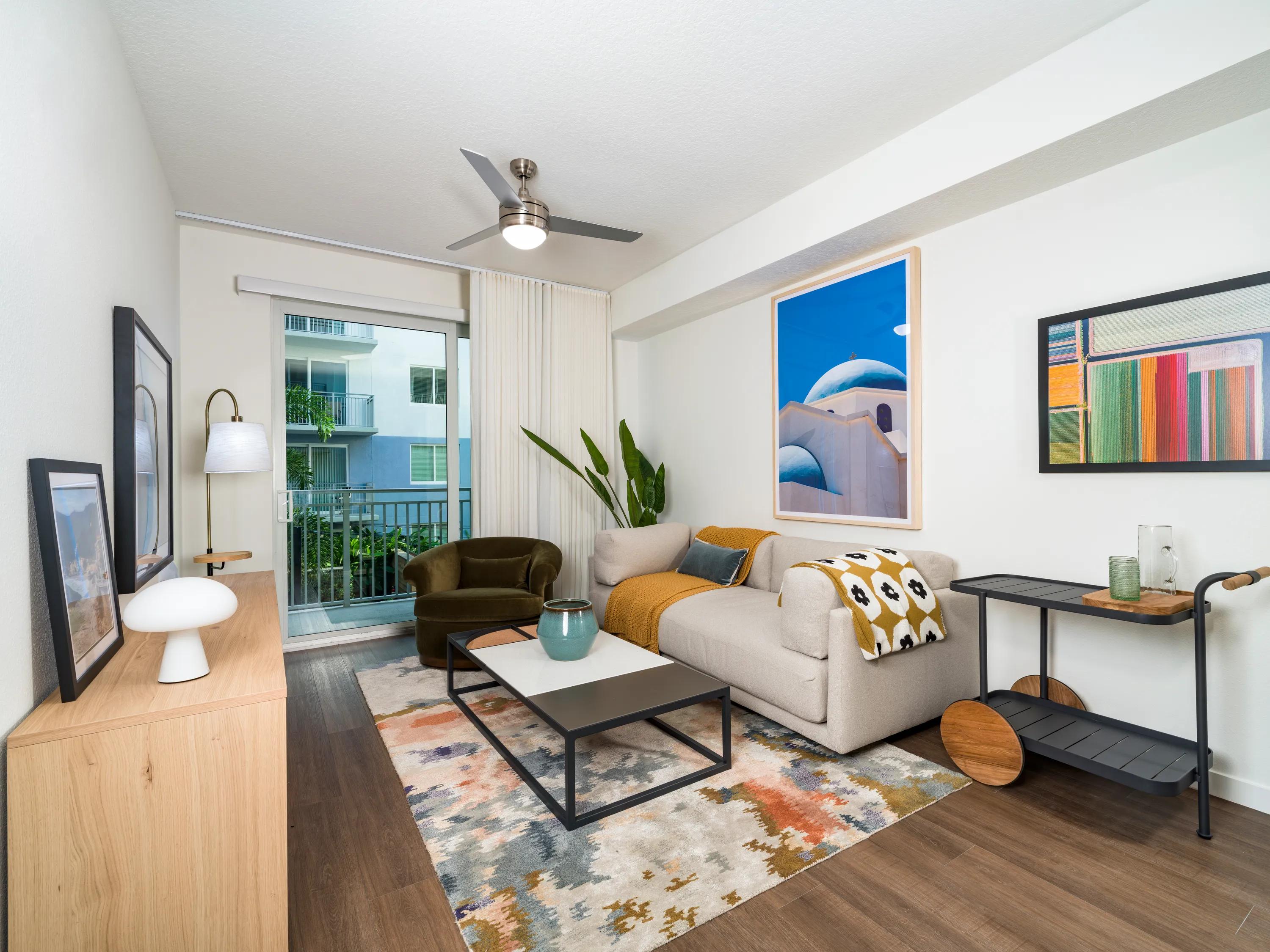 Open-concept living room with wood-style flooring, contemporary finishes, abundant natural light, and direct access to a private balcony at Modera Encore apartments in Tampa, FL.