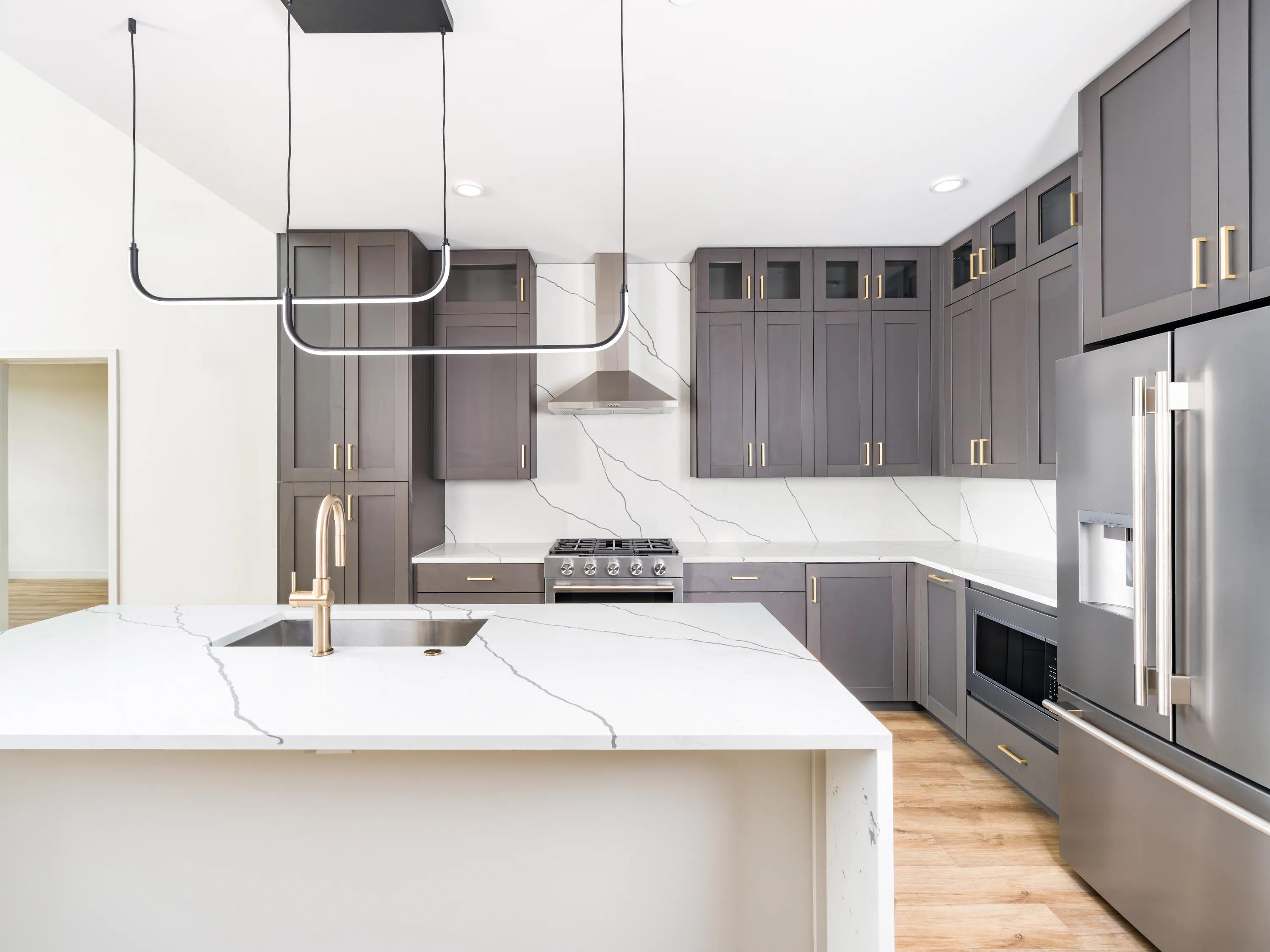 Gourmet kitchen with a quartz waterfall island, full-height gray cabinetry, stainless steel appliances, a tile backsplash, and designer pendant lighting at Modera Second Avenue apartments in Denver, CO.