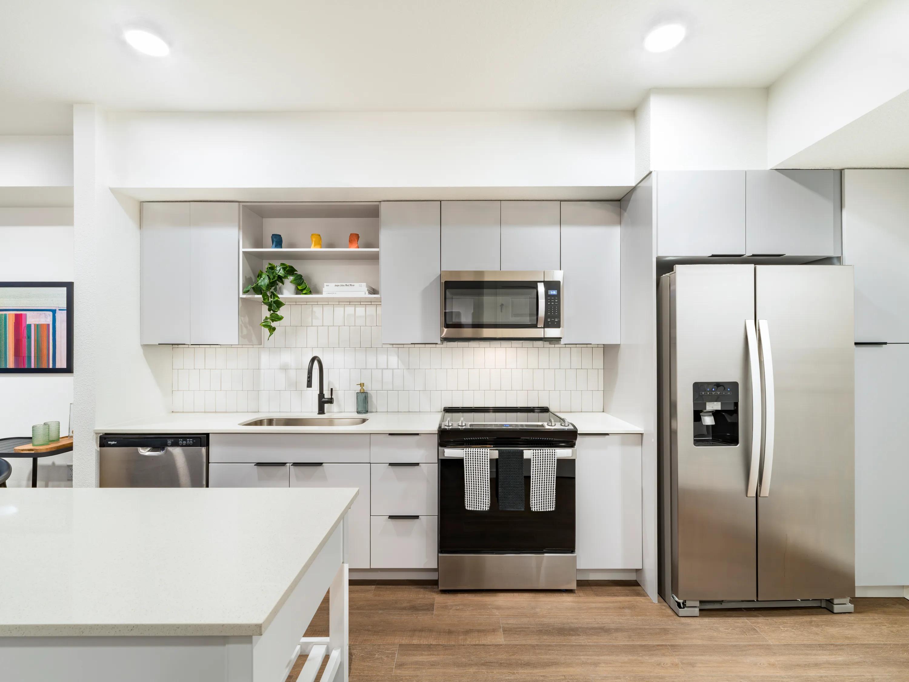Light finish kitchen with soft gray cabinetry, quartz countertops, stainless steel appliances, matte black fixtures, and a tile backsplash in Tampa, FL