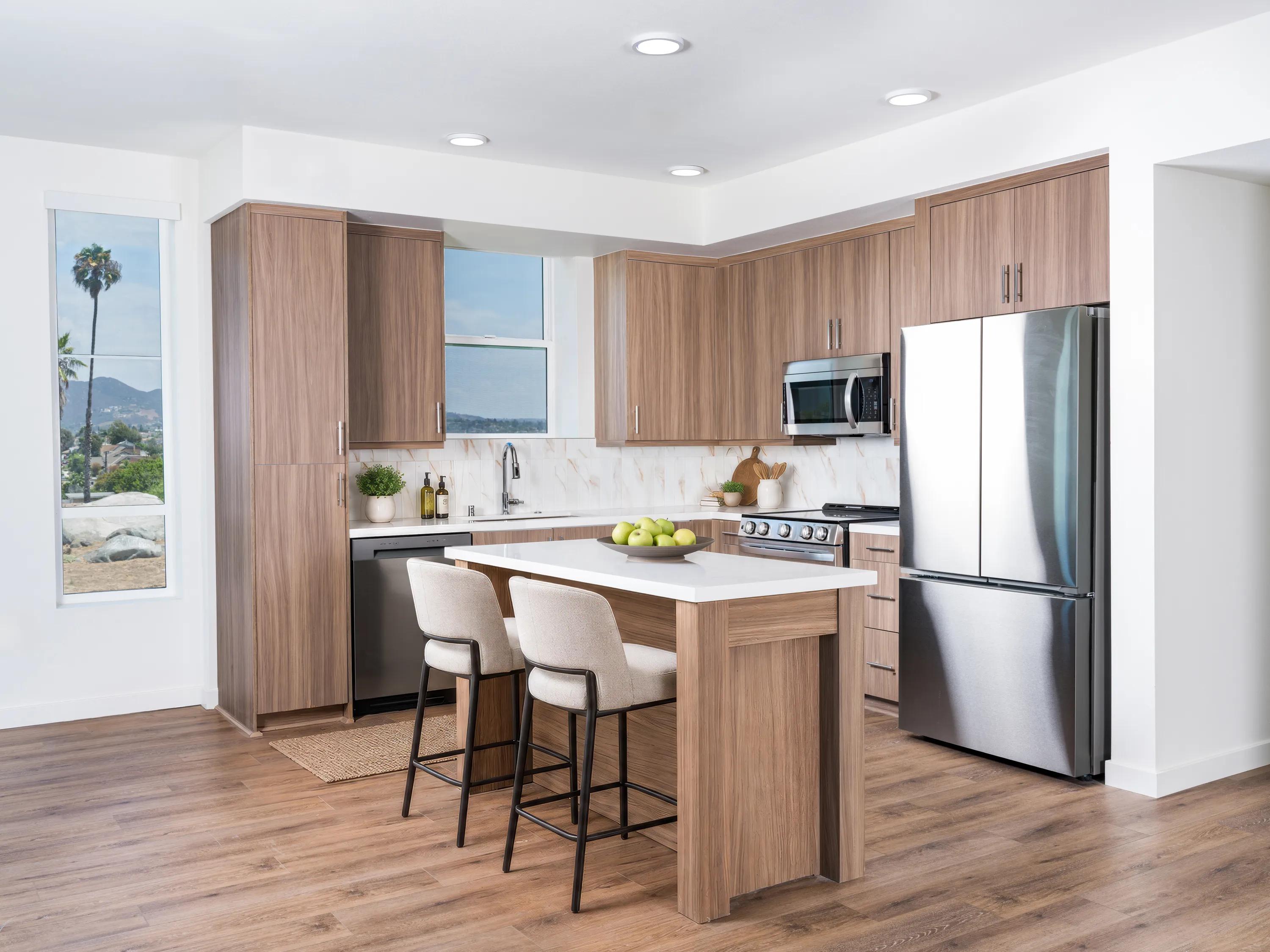 Premium finish kitchen with quartz countertops, wood-grain cabinetry, stainless steel appliances, a large island with seating, and wood-style flooring at Modera Melrose apartments for rent in Oceanside, CA.