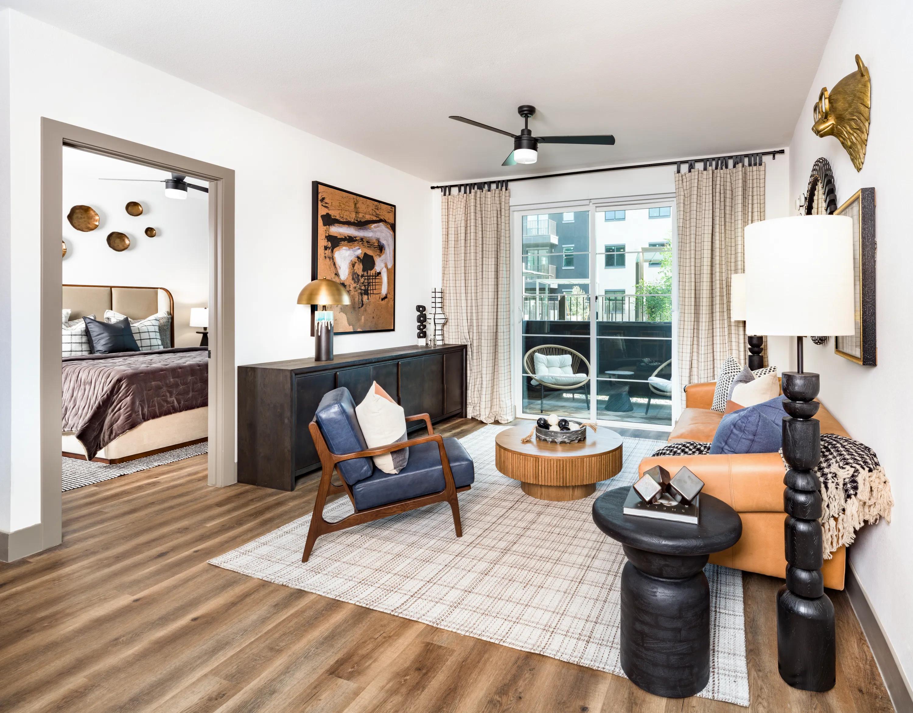 Spacious living room with contemporary furnishings, oversized windows, wood-style plank flooring, and a private balcony connection in apartments in Chandler, AZ.