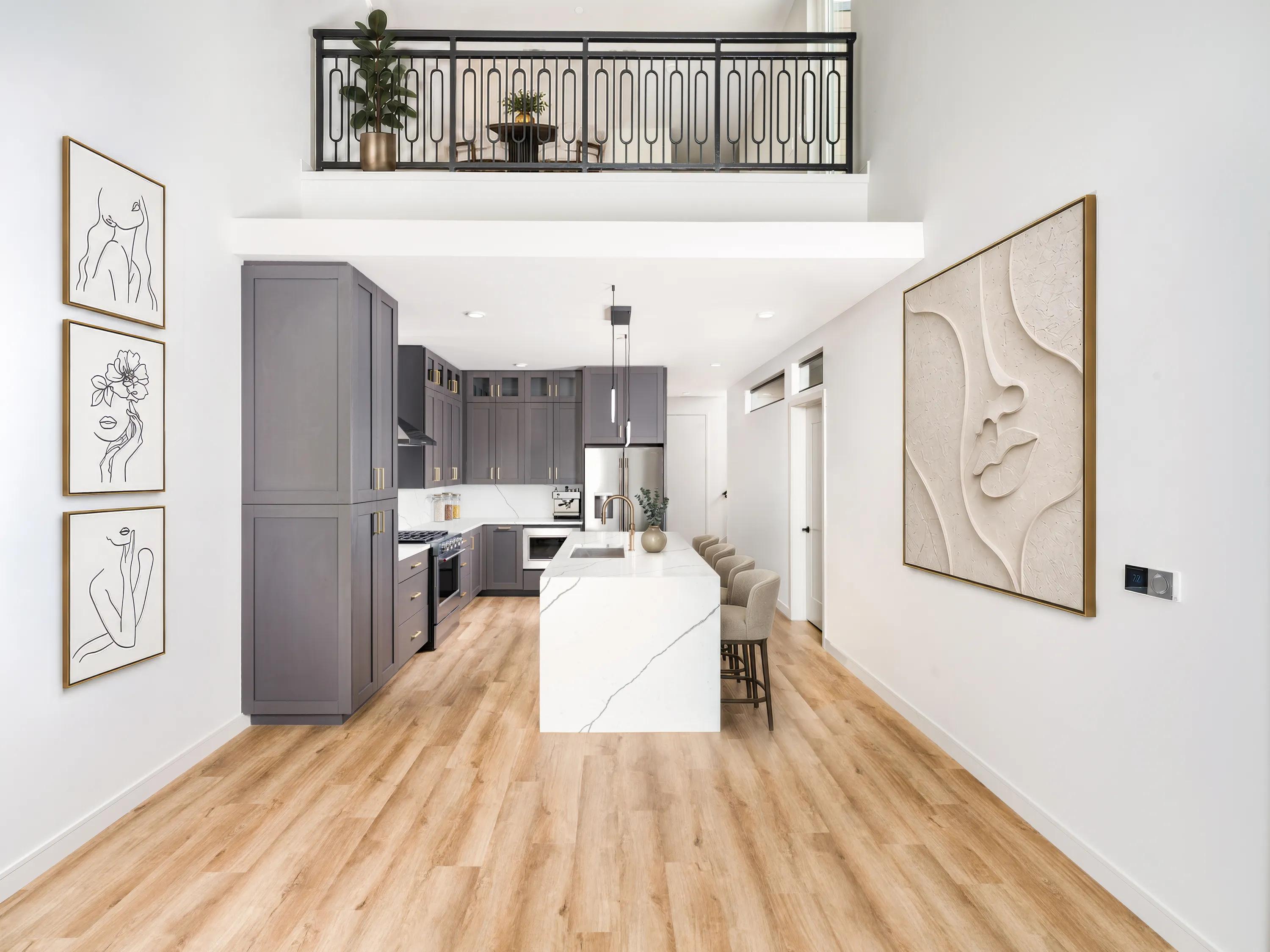Two-story apartment home with a loft overlooking an open-concept kitchen, featuring a quartz waterfall island, gray cabinetry, stainless steel appliances, and wood-style flooring at Modera Second Avenue apartments in Denver, CO.