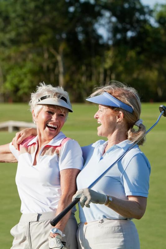 Two mature women smiling while holding a golf club
