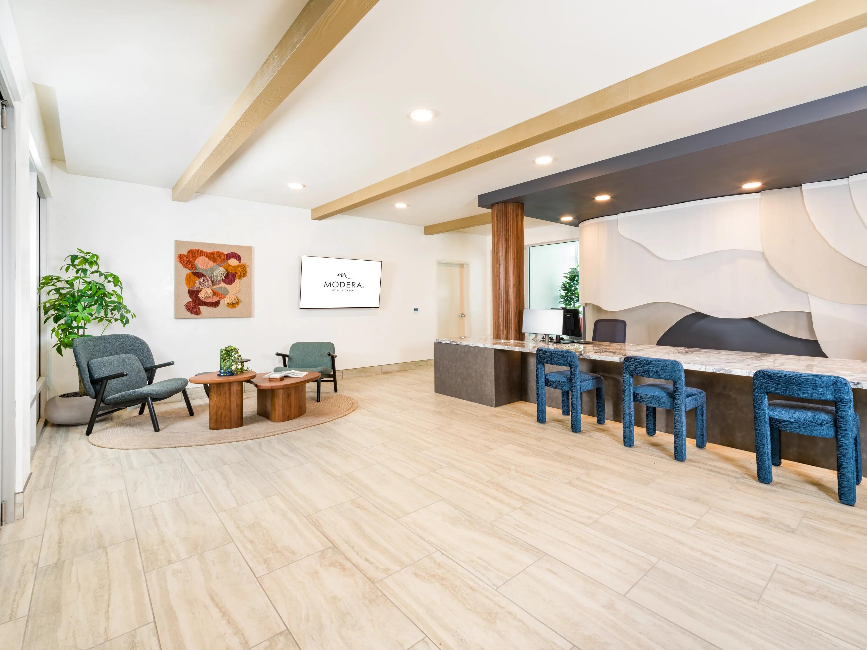 Contemporary resident lobby with lounge seating, a hospitality-inspired reception desk, designer lighting, wood-accent beams, and modern finishes at Modera Melrose apartments for rent in Oceanside, CA.