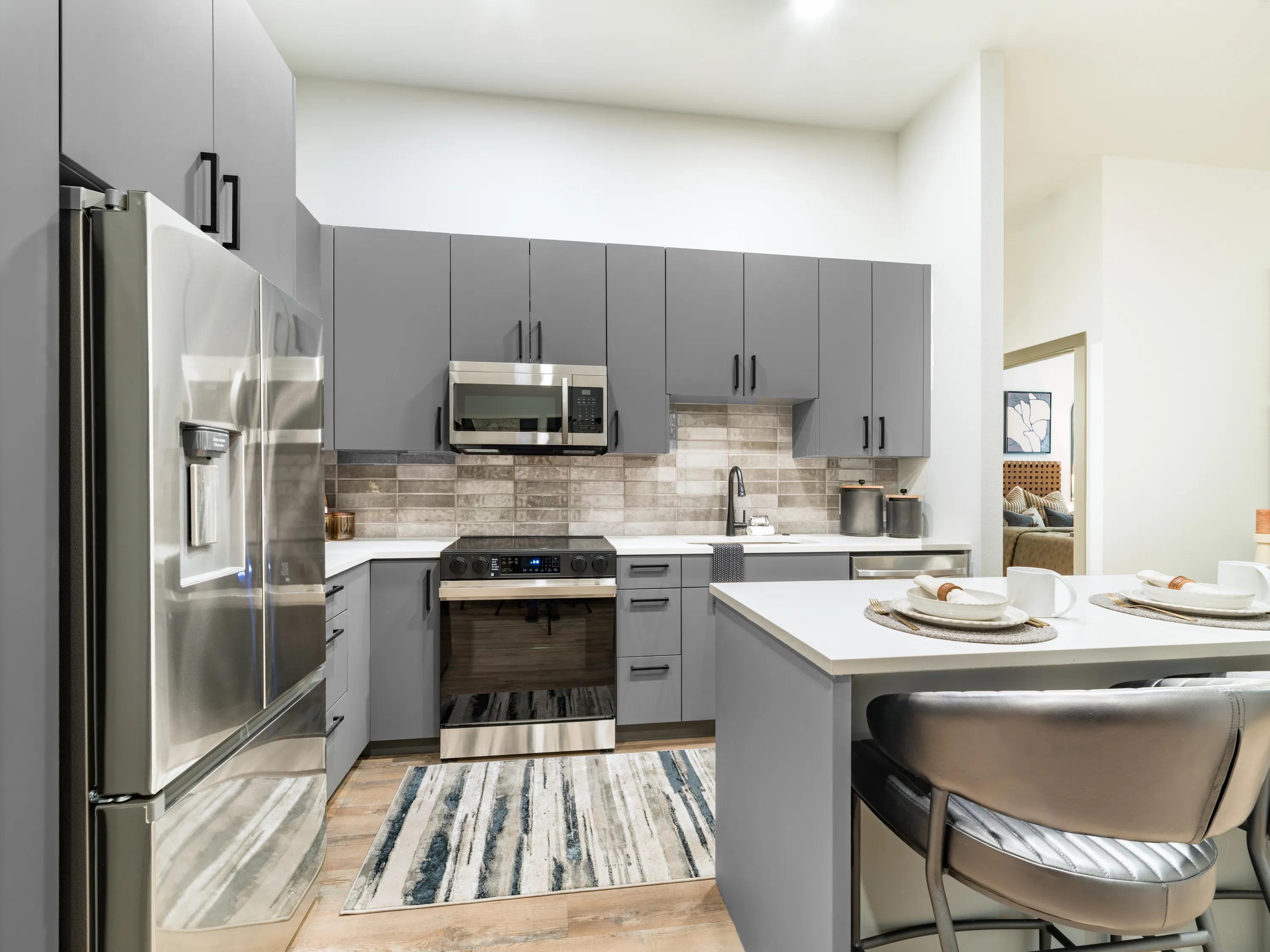 Modern gourmet kitchen with quartz countertops, gray custom cabinetry, stainless steel appliances, tile backsplash, and an eat-in island in apartments in Chandler, AZ.