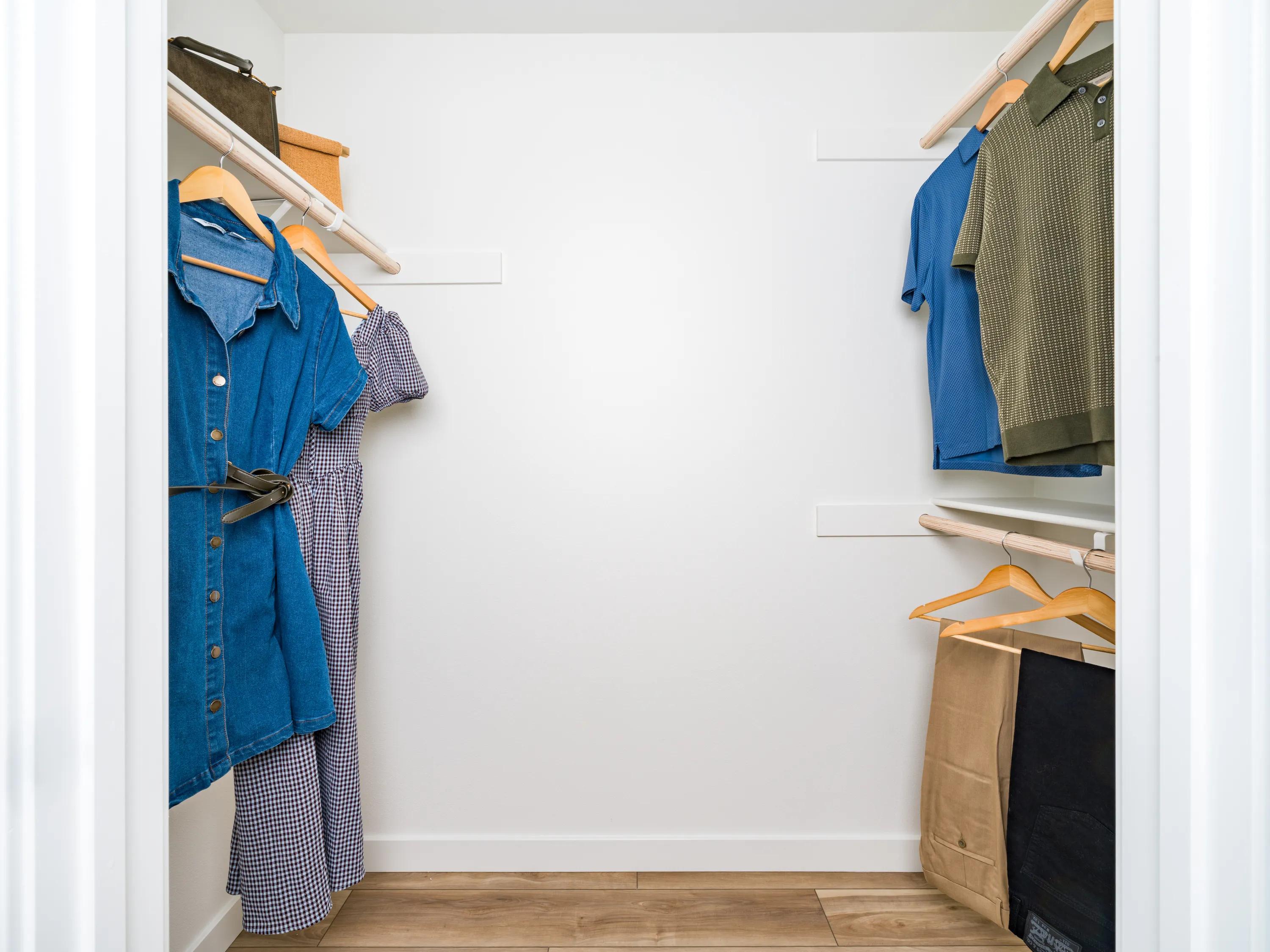 Spacious walk-in closet with built-in hanging storage, open shelving, and wood-style flooring at Modera Melrose apartments for rent in Oceanside, CA.