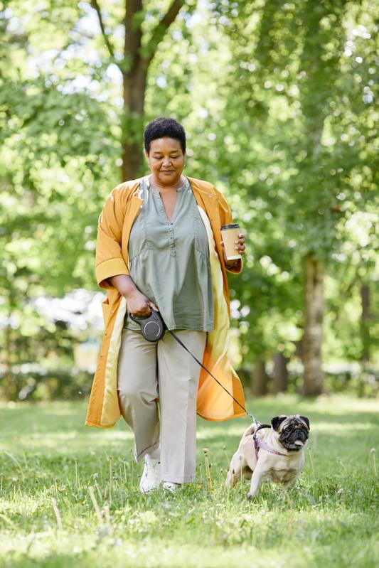 woman walking pug and holding coffee outside in park near the avens at dedham station apartments in ma