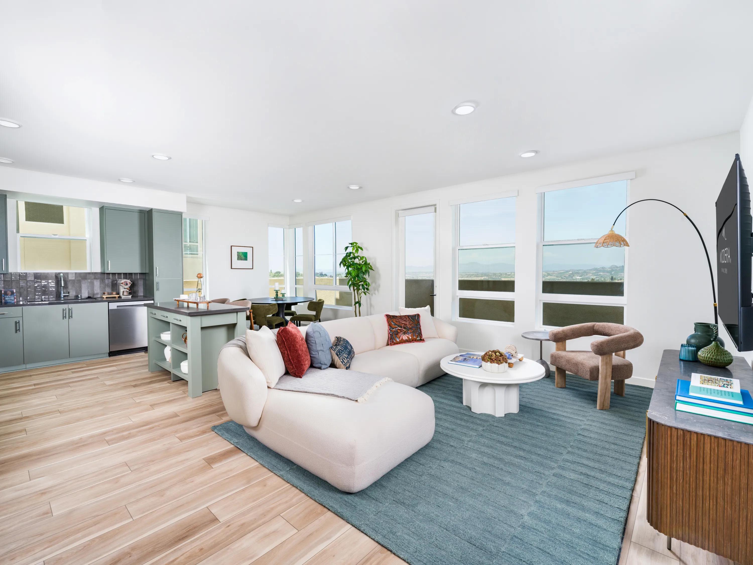 Bright open-concept apartment home with a spacious living room, oversized windows, contemporary kitchen with island seating, and wood-style flooring at Modera Melrose apartments for rent in Oceanside, CA