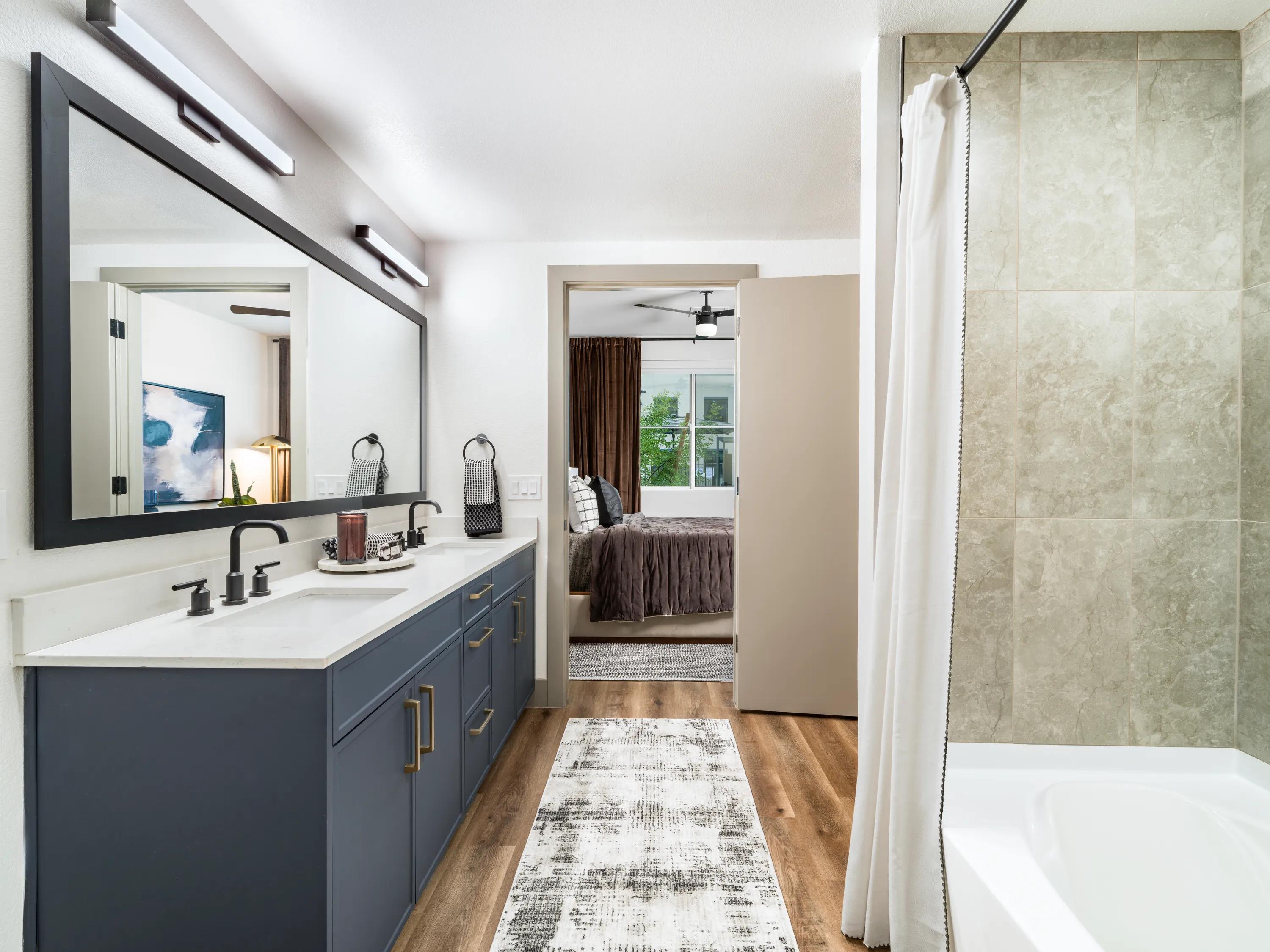 Designer bathroom with dual-sink vanity, quartz countertop, modern cabinetry, large framed mirror, and tiled shower in apartments in Chandler, AZ.