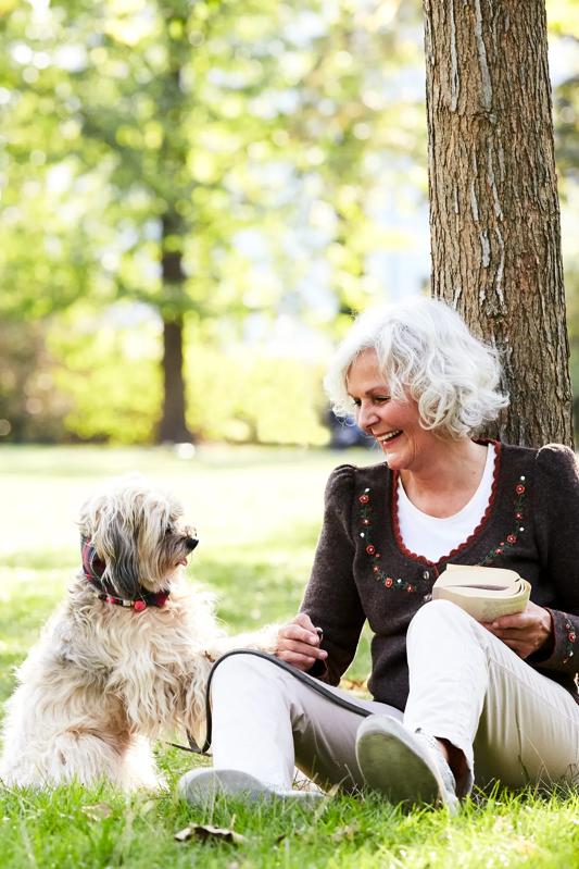 portrait of a content and happy senior woman in her late 60is enjoying time with her Chinese Crested Powder Puff dog sitting on the lawn in a park in autumn modera second avenue apartments in denver co
