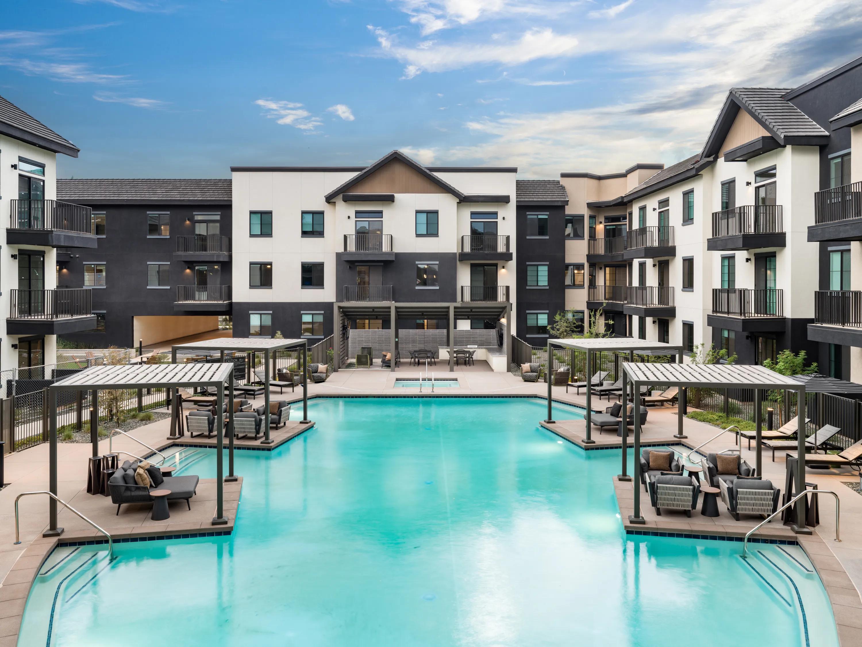 Wide view of the resort-style swimming pool with private cabanas, lounge seating, landscaped courtyards, and contemporary apartment buildings at Modera Chandler apartments in Chandler, AZ.