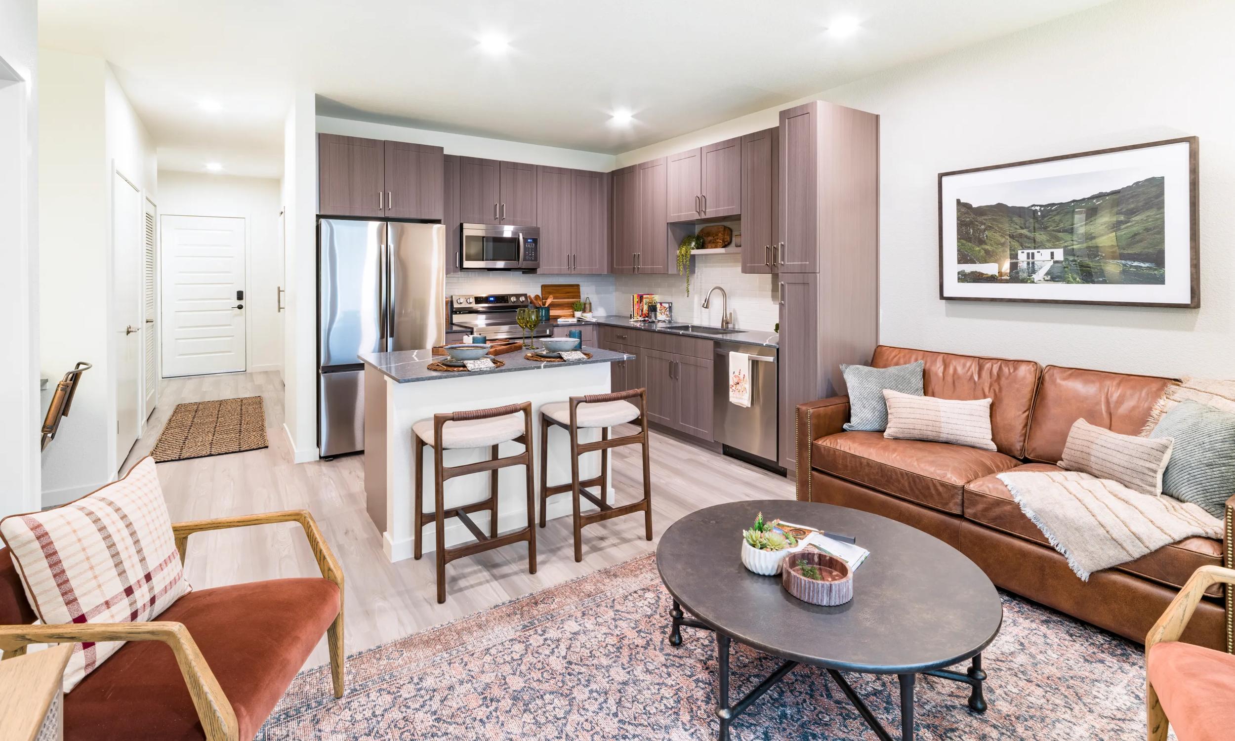 Modern kitchen with elegant dark cabinetry, a sleek island, and chic bar stools, complemented by a stylish nook with a round mirror and cozy desk.