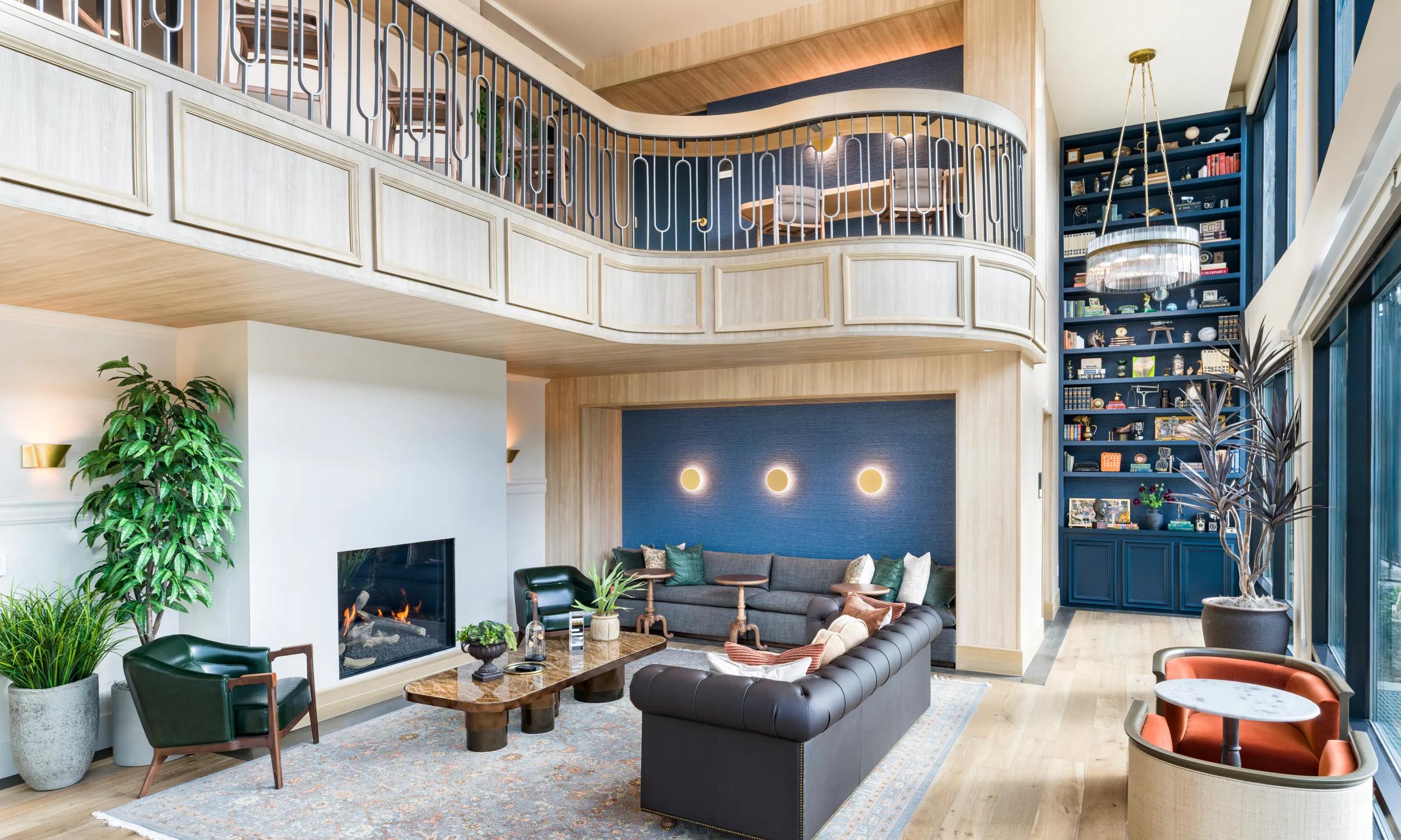 Luxurious living room with a cozy fireplace, elegant high ceiling, and grand bookshelf. Abundant natural light enhances the sophisticated decor and plush seating arrangement.