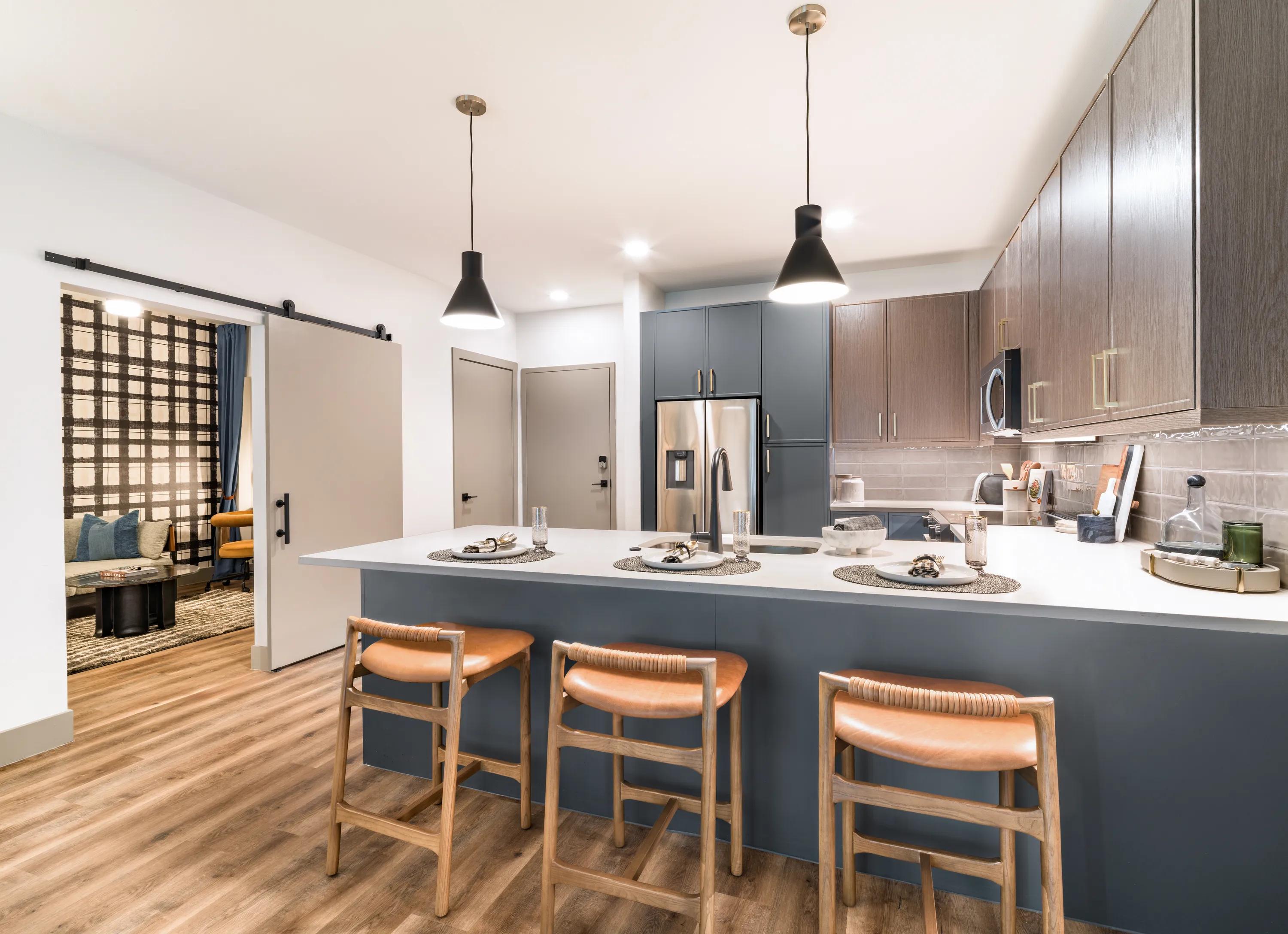 Open-concept apartment kitchen with a large quartz island, bar seating, custom cabinetry, stainless steel appliances, and wood-style plank flooring in apartments in Chandler, AZ.