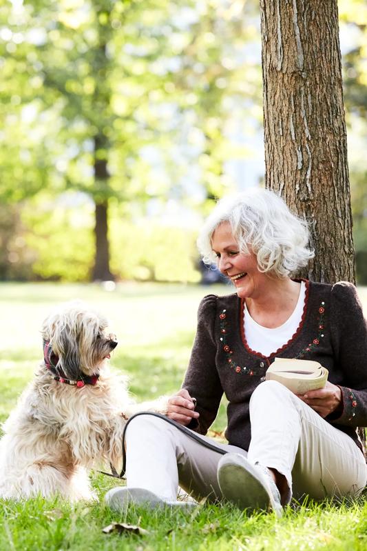 mature woman with dog sitting outside in a park reading a book