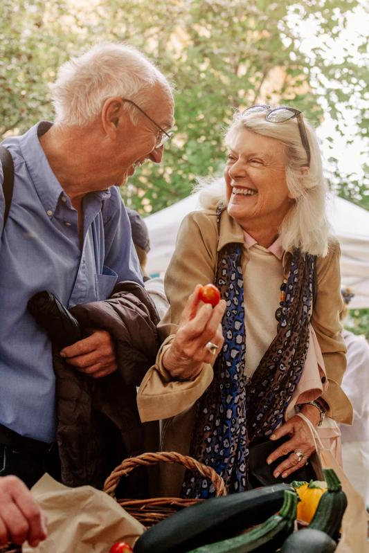 mature couple shopping at farmers market looking at produce and smiling nearby modera marmalade