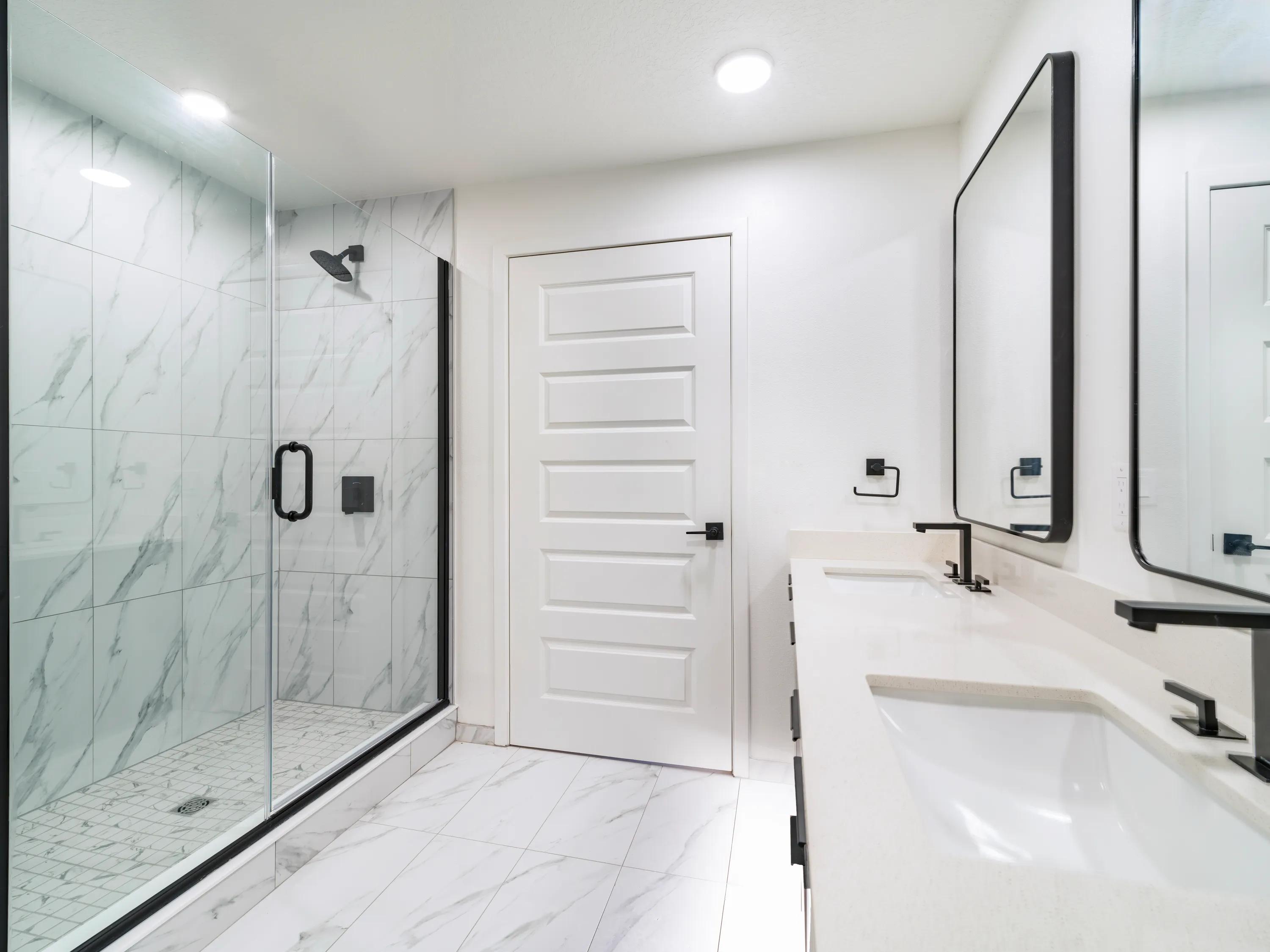 Contemporary bathroom with a double-sink vanity, quartz countertop, frameless glass walk-in shower, marble-inspired tile, and modern black fixtures at Modera Encore apartments in Tampa, FL.