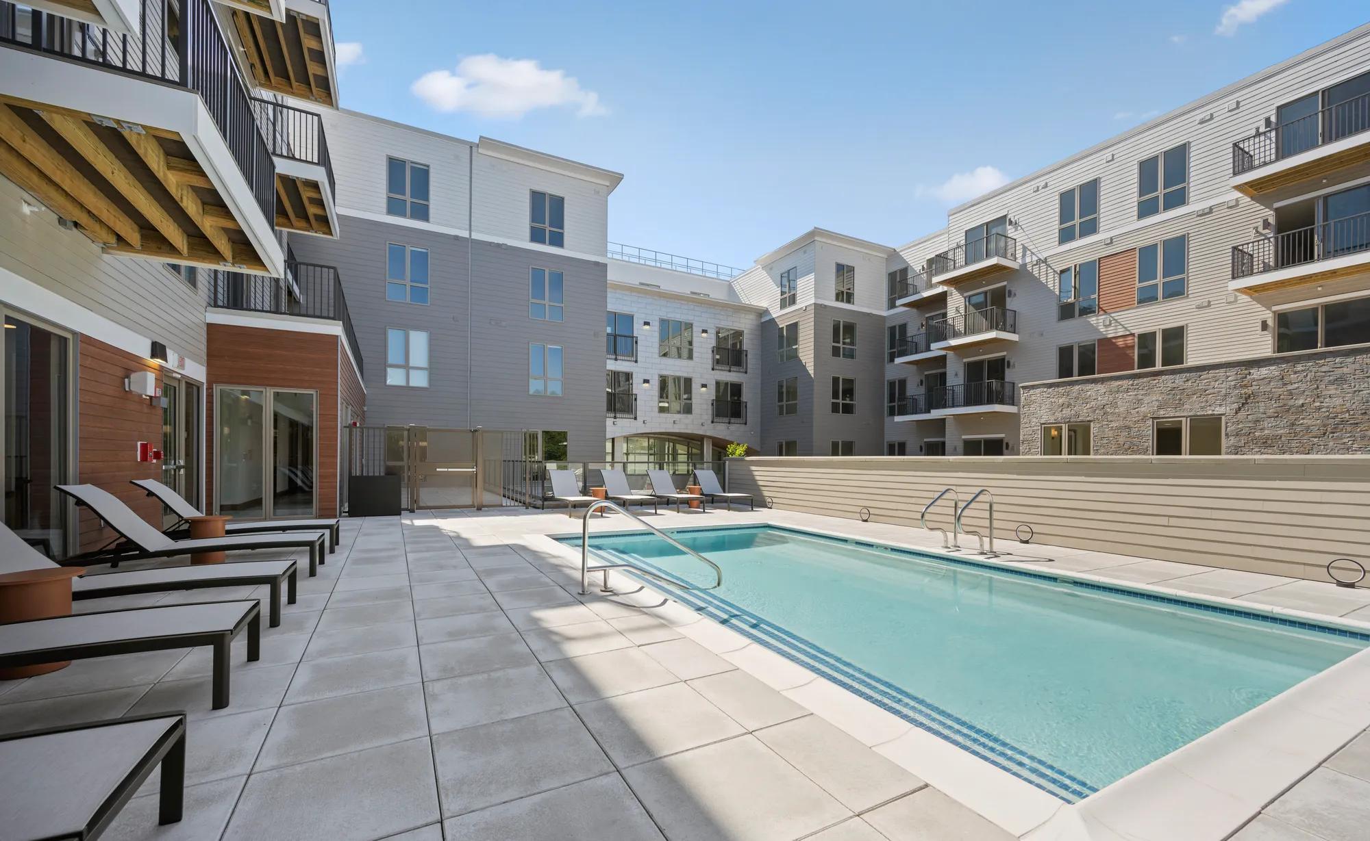pool and sundeck looking towards building with windows at modera newton apartment homes for rent in ma