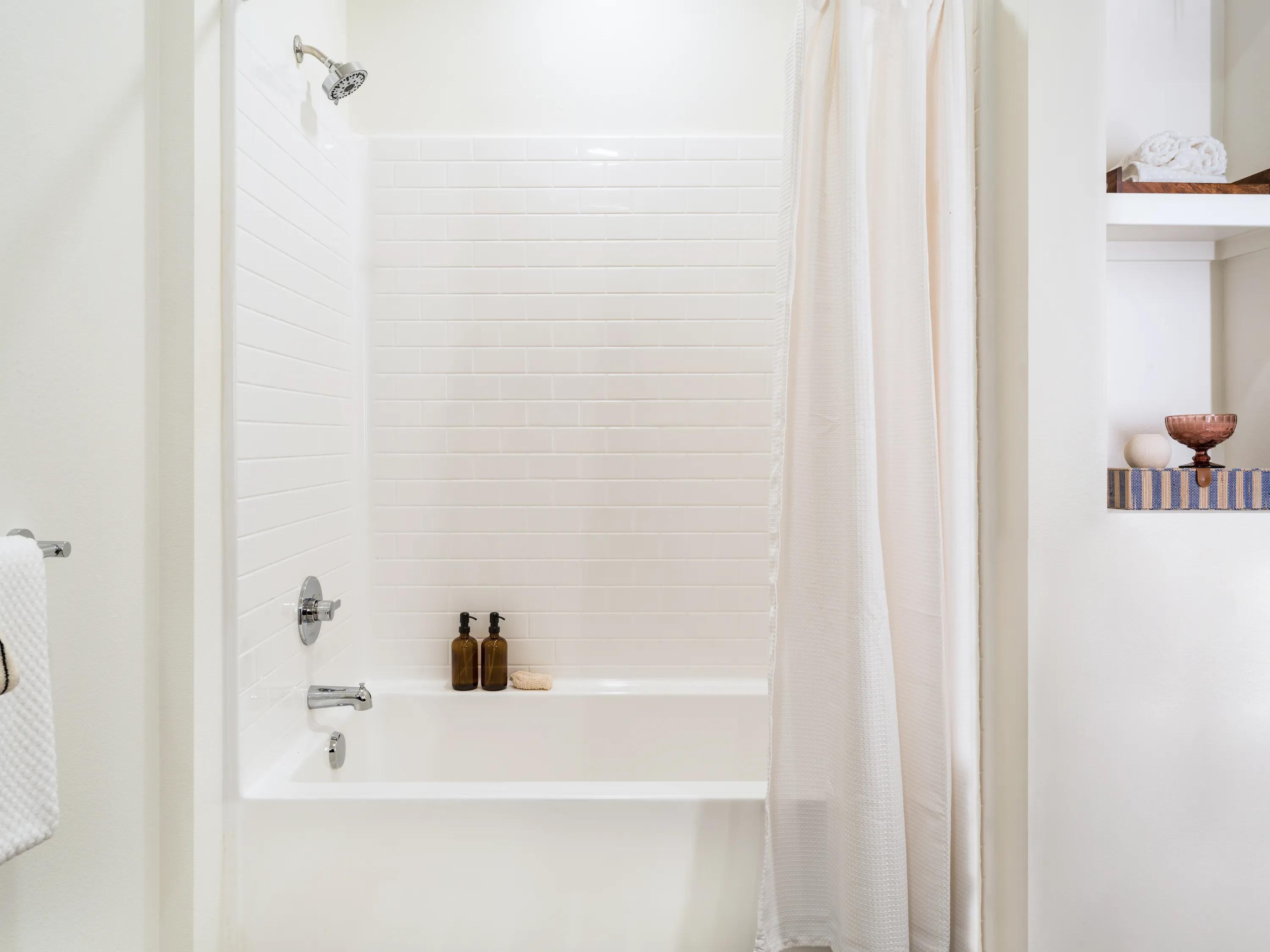Bright bathroom with a soaking tub and shower combination, white subway tile surround, built-in shelving, and contemporary fixtures at Modera Melrose apartments for rent in Oceanside, CA.