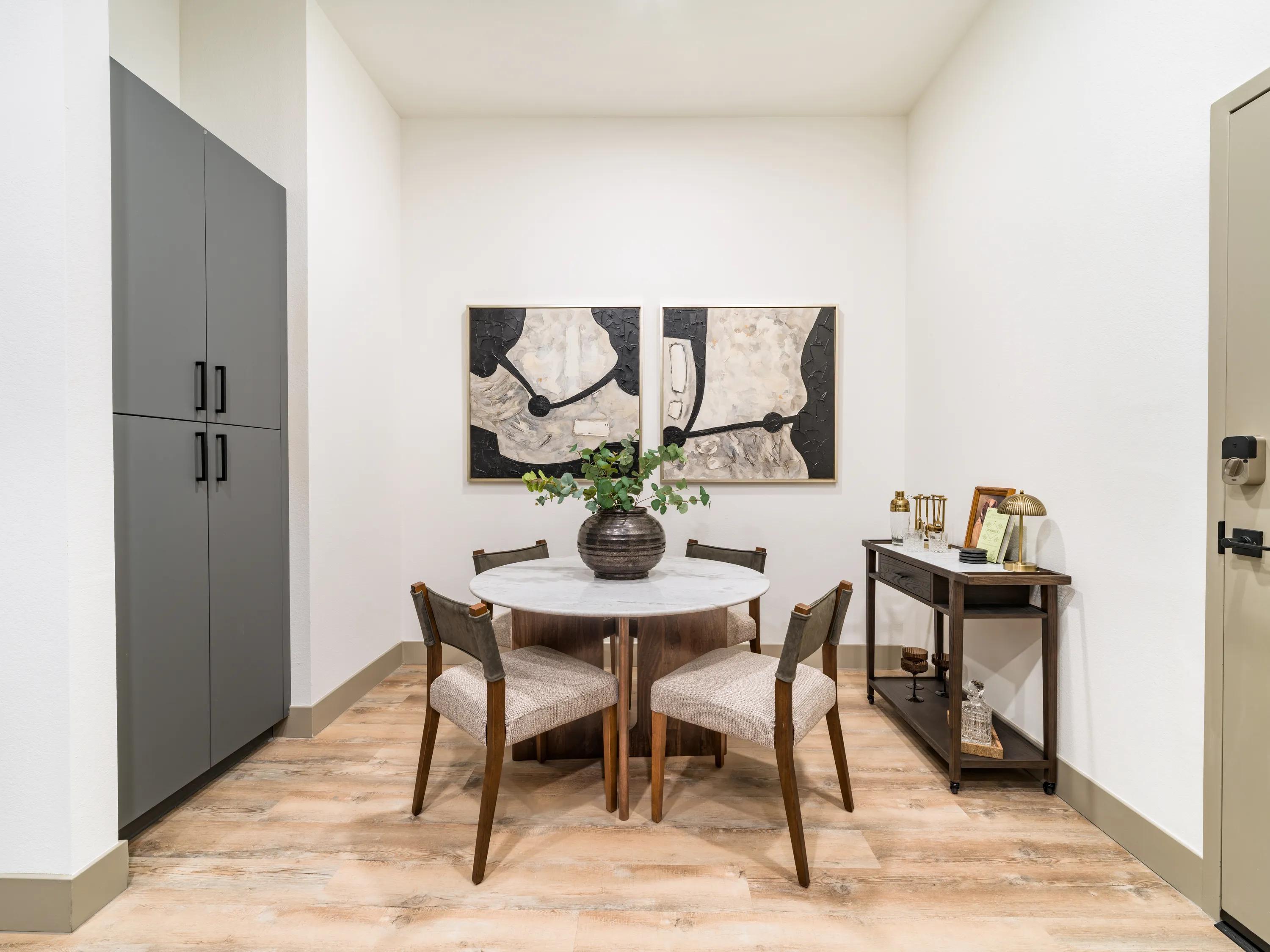 Apartment dining area with a round dining table, modern artwork, built-in storage cabinetry, and wood-style plank flooring in apartments in Chandler, AZ.