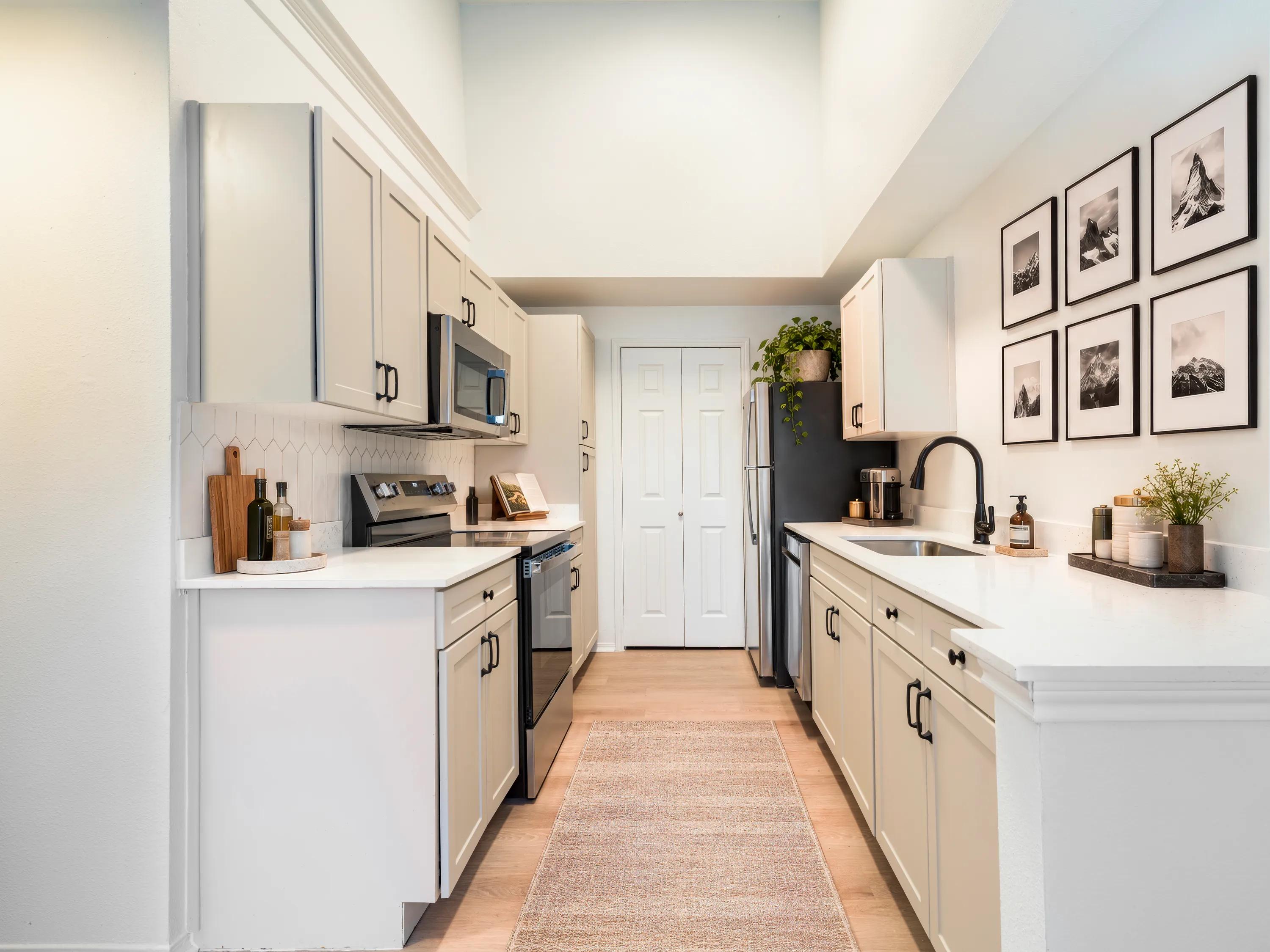 Light finish kitchen with white shaker-style cabinetry, quartz countertops, stainless steel appliances, a geometric tile backsplash, and wood-style flooring at Alister Sunset Valley apartments in Austin, TX.