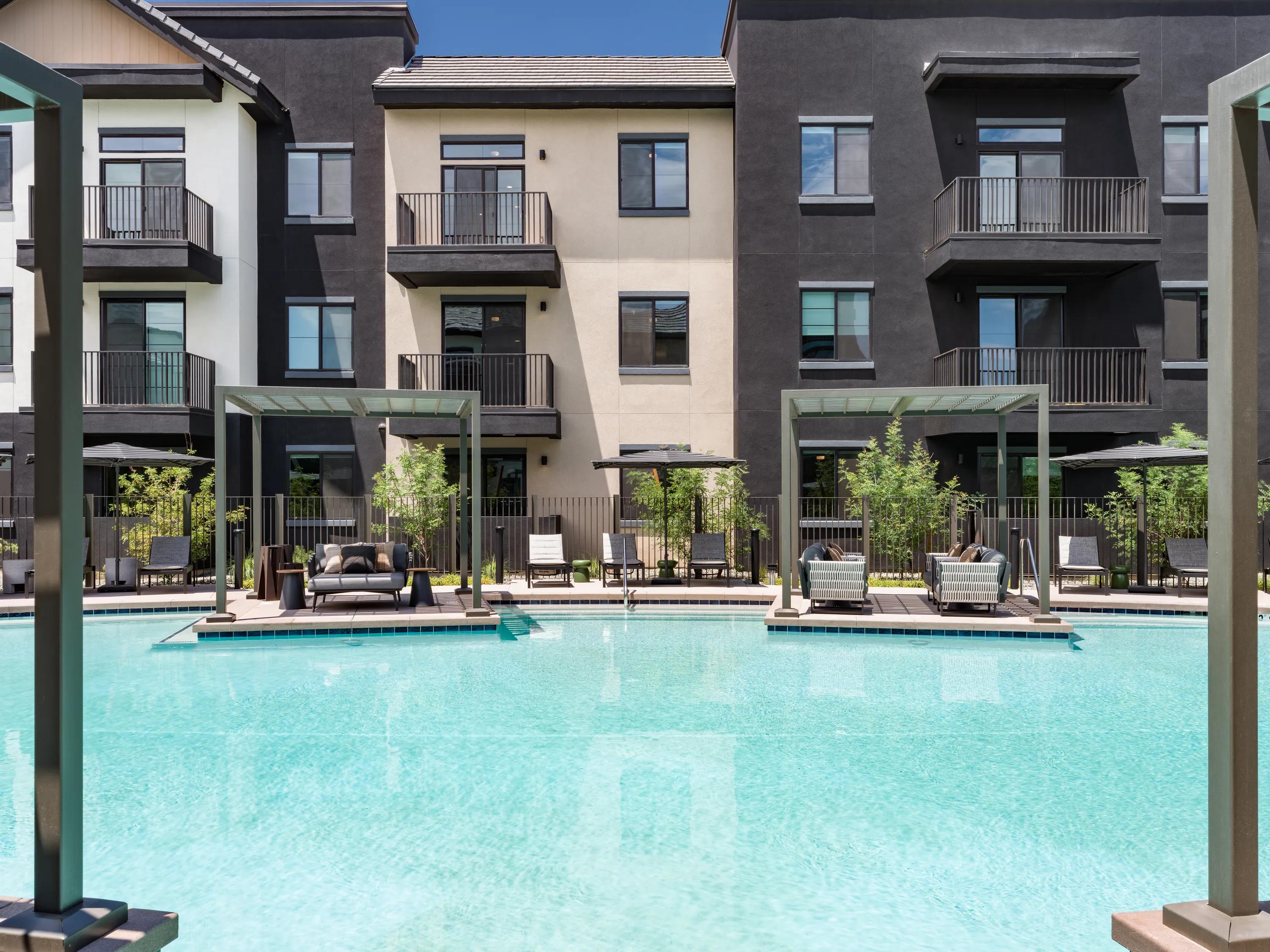 Resort-style swimming pool with private cabanas, lounge seating, landscaped surroundings, and apartment buildings at Modera Chandler apartments in Chandler, AZ.