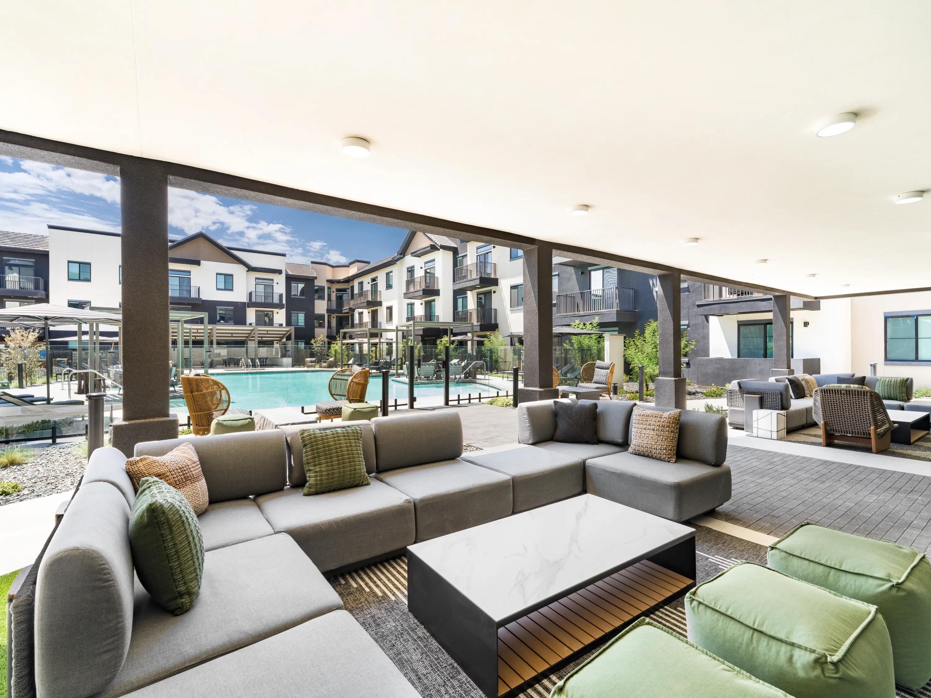 Covered outdoor lounge with sectional seating, modern furnishings, and views of the resort-style pool at Modera Chandler apartments in Chandler, AZ.