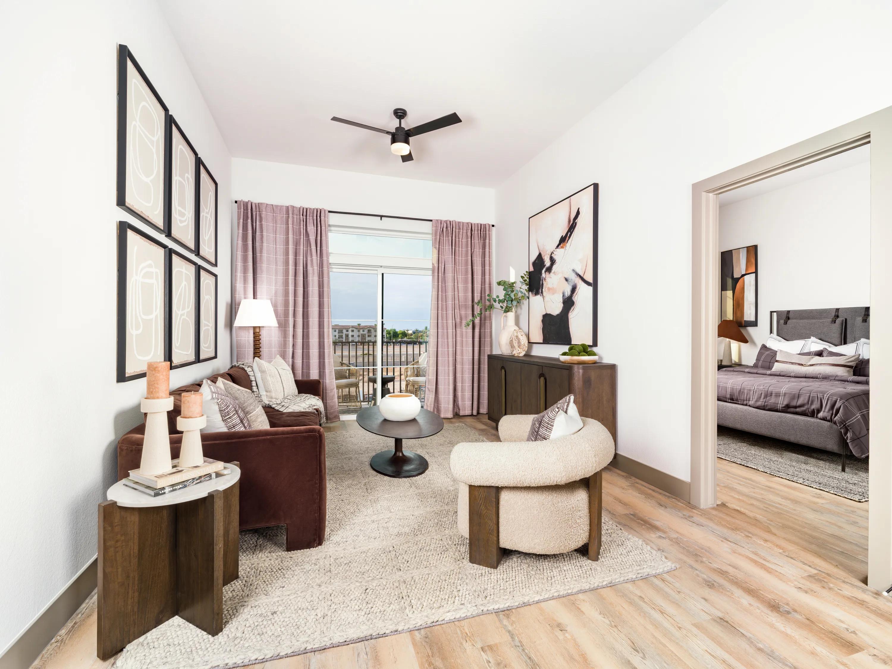 Contemporary living room with wood-style plank flooring, modern furnishings, oversized windows, and a private balcony view in apartments in Chandler, AZ.