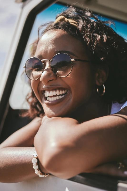 woman looking out window of car smiling while wearing sunglasses