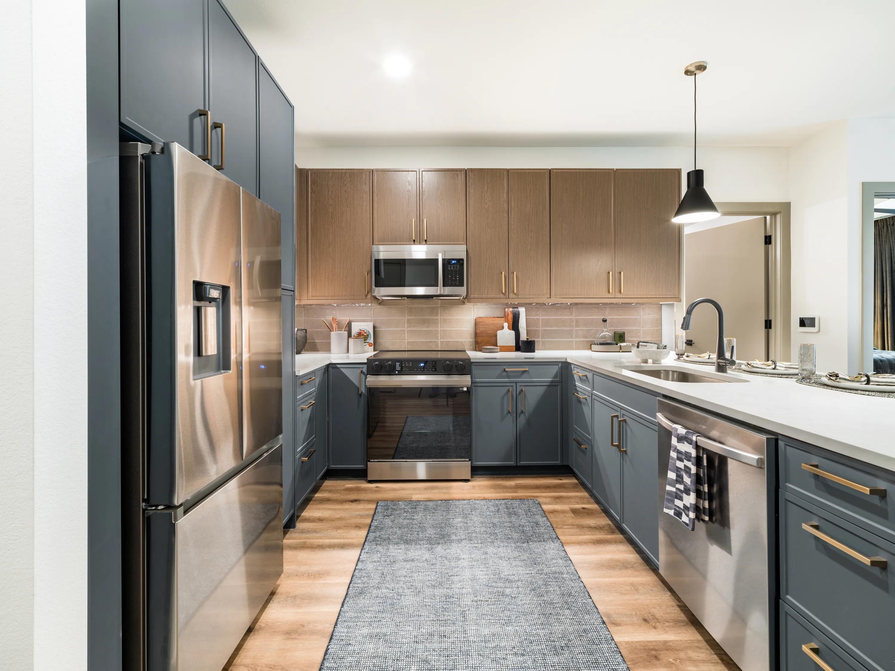 Spacious gourmet kitchen with quartz countertops, custom blue and wood-tone cabinetry, stainless steel appliances, pendant lighting, and wood-style plank flooring in apartments in Chandler, AZ.