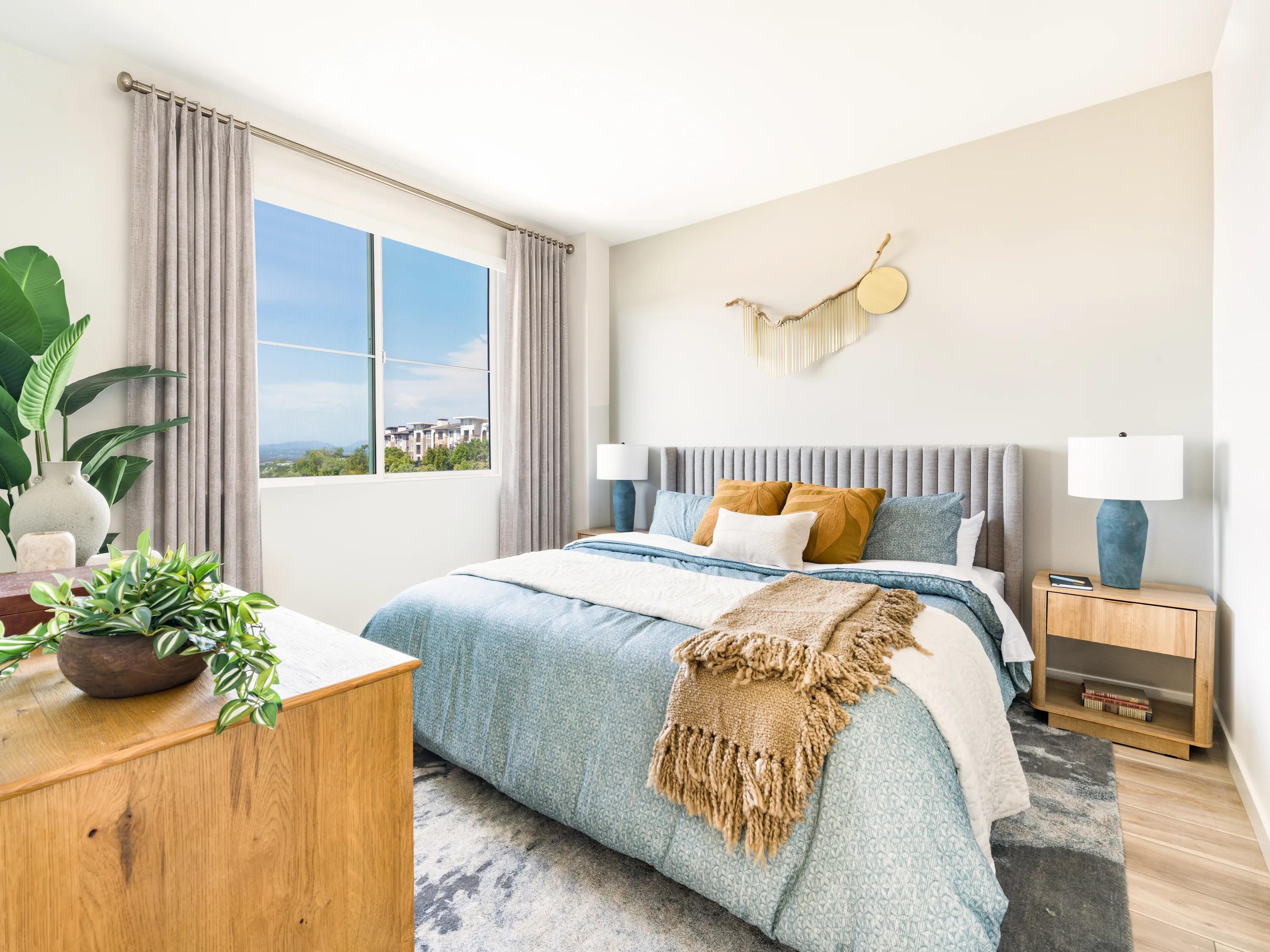 Primary bedroom with oversized windows, plush carpeting, contemporary furnishings, and abundant natural light at Modera Melrose apartments for rent in Oceanside, CA.