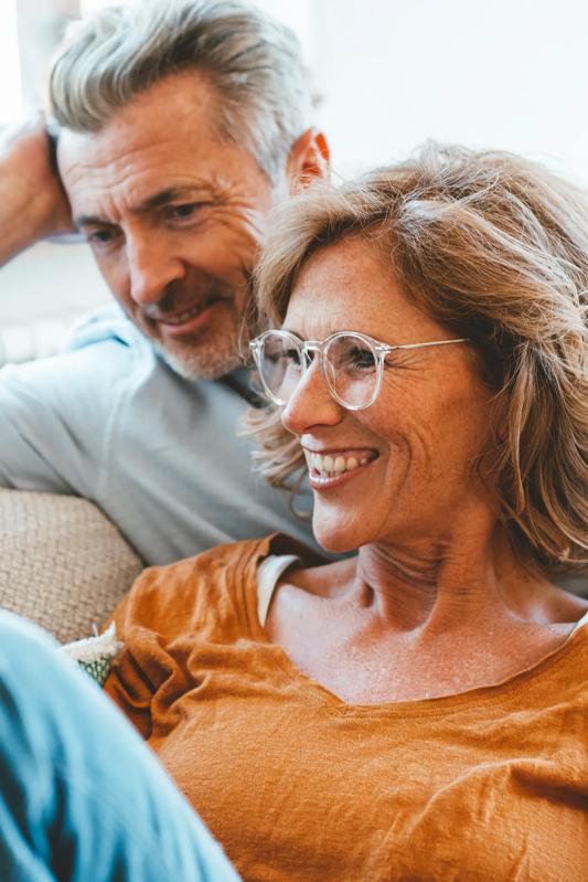 mature couple sitting on couch smiling in the same direction looking at a computer